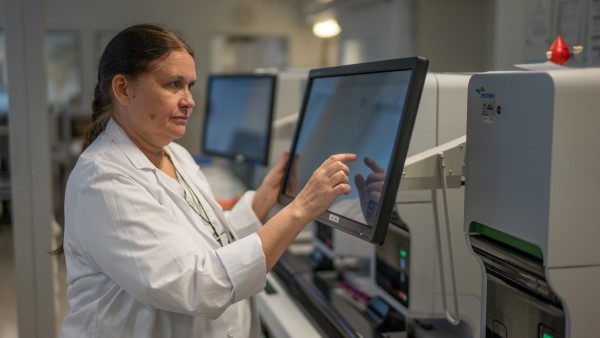 Bilde av Karin Toska som står foran en maskin på et laboratorium