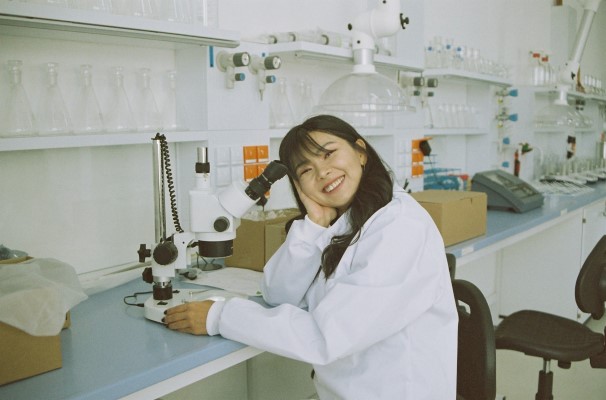 Kvinne smiler og sitter ved pulten på et laboratorium